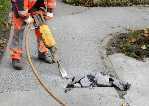 Worker breaking damaged concrete with a demolition hammer