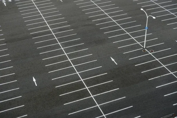 Overhead view of a striped asphalt parking lot with marked spaces and directional arrows